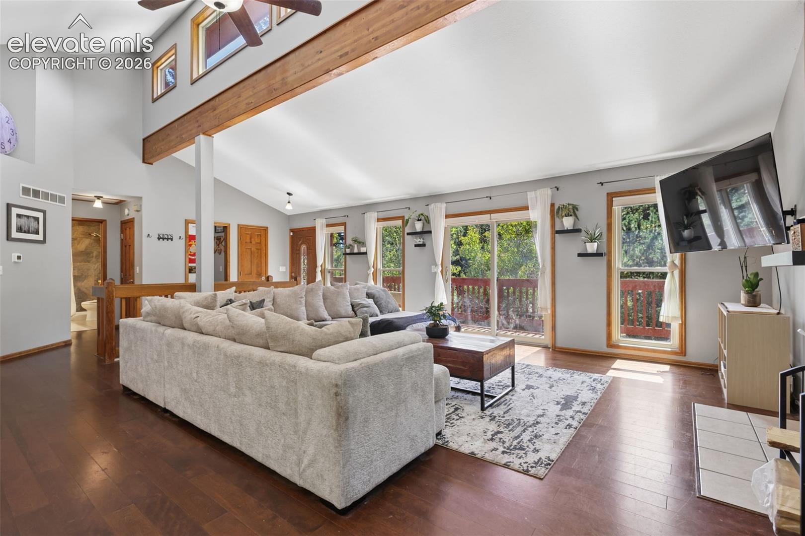 Vaulted ceiling with exposed wood beam, hardwood flooring, ceiling fan, and sliding glass doors with outdoor access
