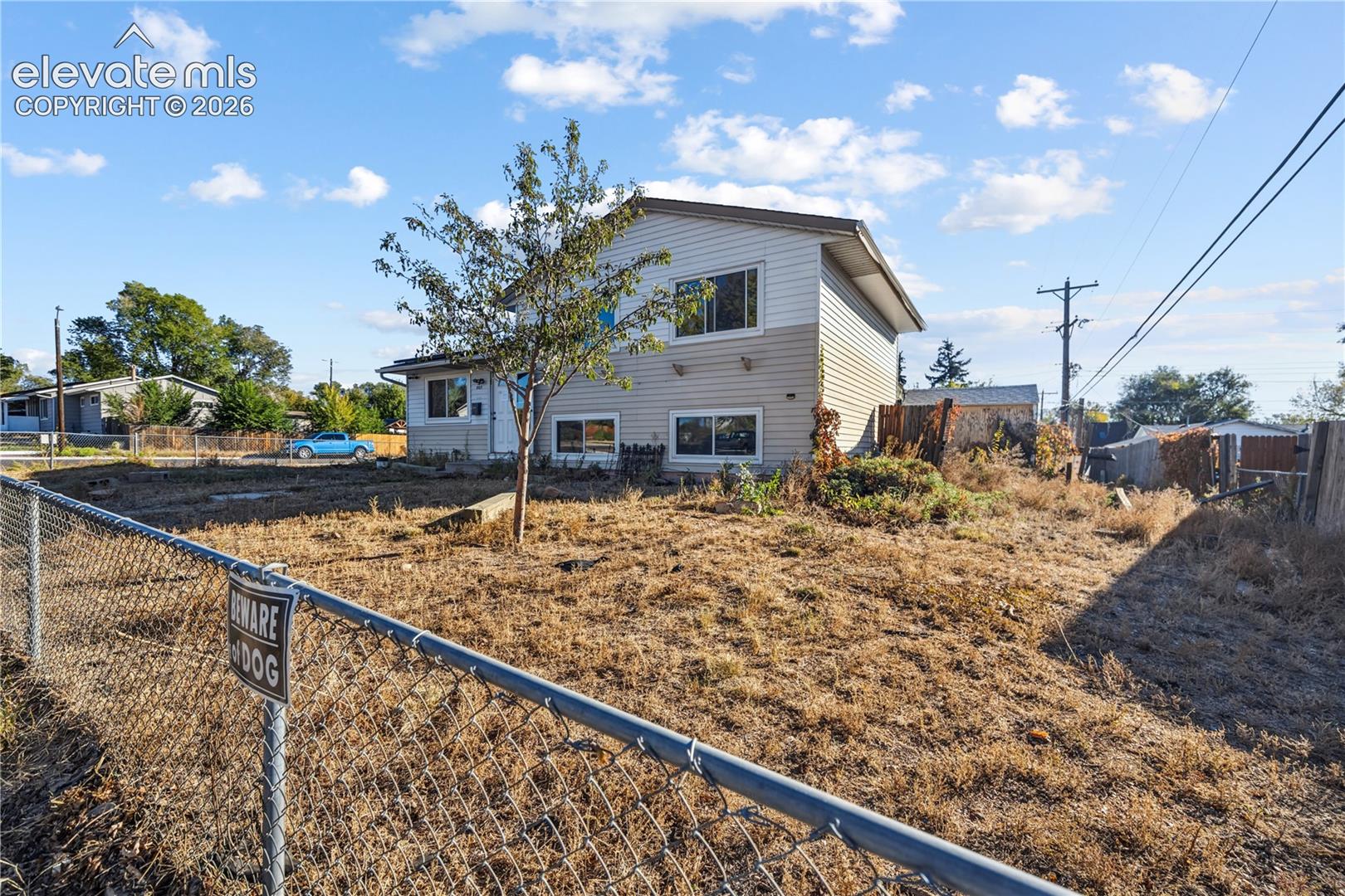 Split-level residence featuring horizontal siding, double-pane windows, and chain-link perimeter fencing