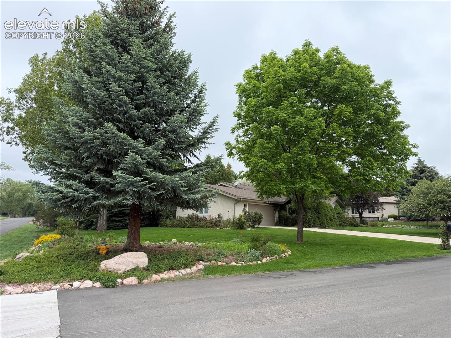 Residential property featuring a sprawling green lawn, mature trees, and landscaping with decorative rocks