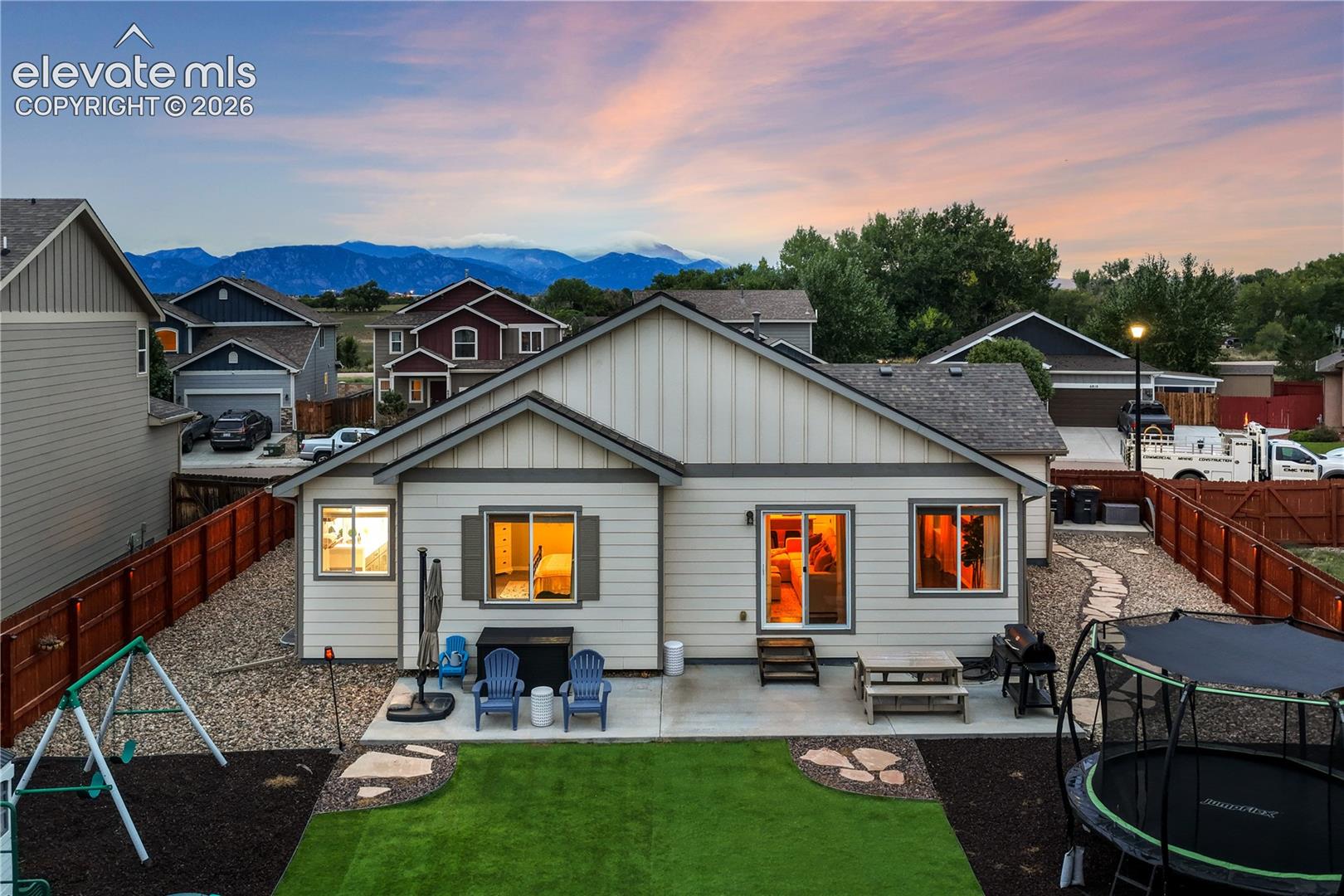 Rear exterior with a concrete patio, artificial turf, and a wood privacy fence
