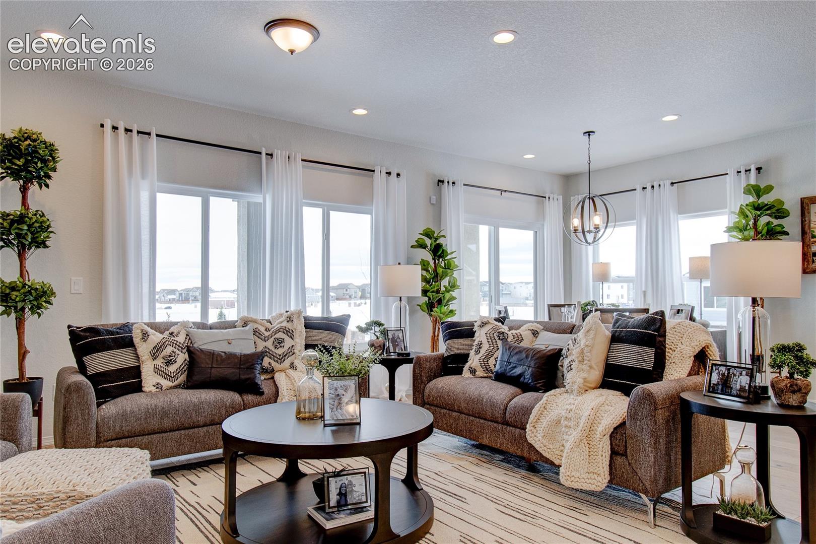 Open-concept interior featuring recessed lighting, large windows with black curtain rods, and a contemporary orb-style chandelier