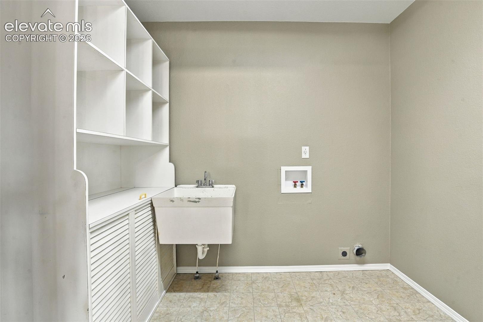 Laundry area with white built-in shelving, white louvered cabinetry, and a utility sink