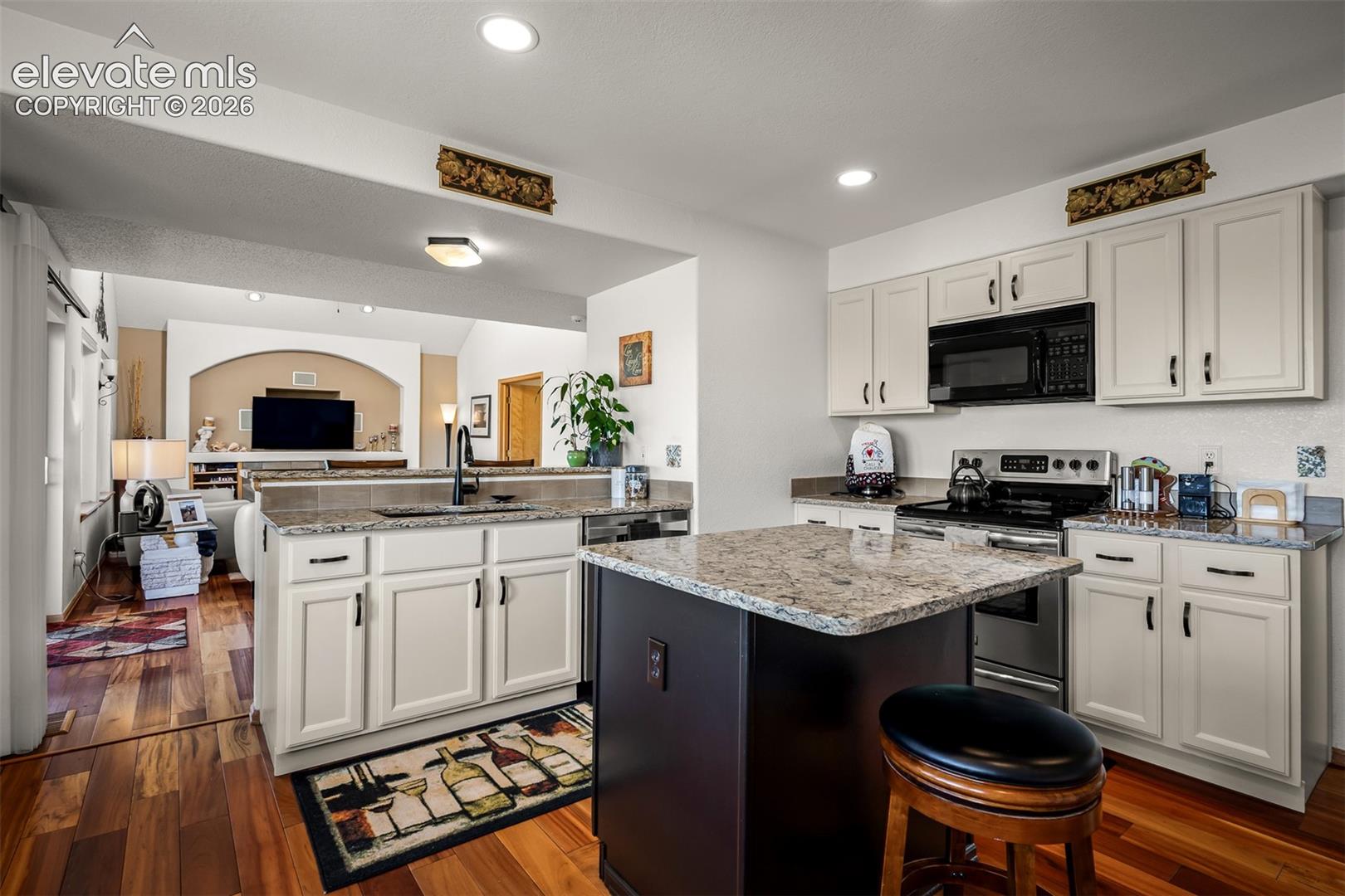 Kitchen featuring light colored cabinetry, quartz countertops, and Brazilian Koa Hardwood flooring.  Looking into family room.