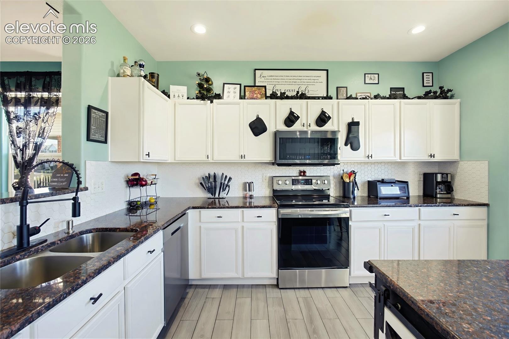 Kitchen featuring white cabinetry, dark speckled countertops, stainless steel appliances, and hexagon tile backsplash