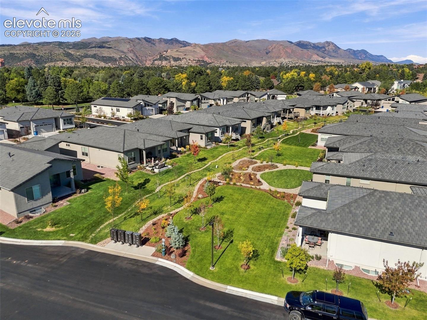 Aerial perspective featuring multi-unit residential structures with composition shingle roofing, integrated landscaping, manicured lawn areas, and prominent mountain backdrop