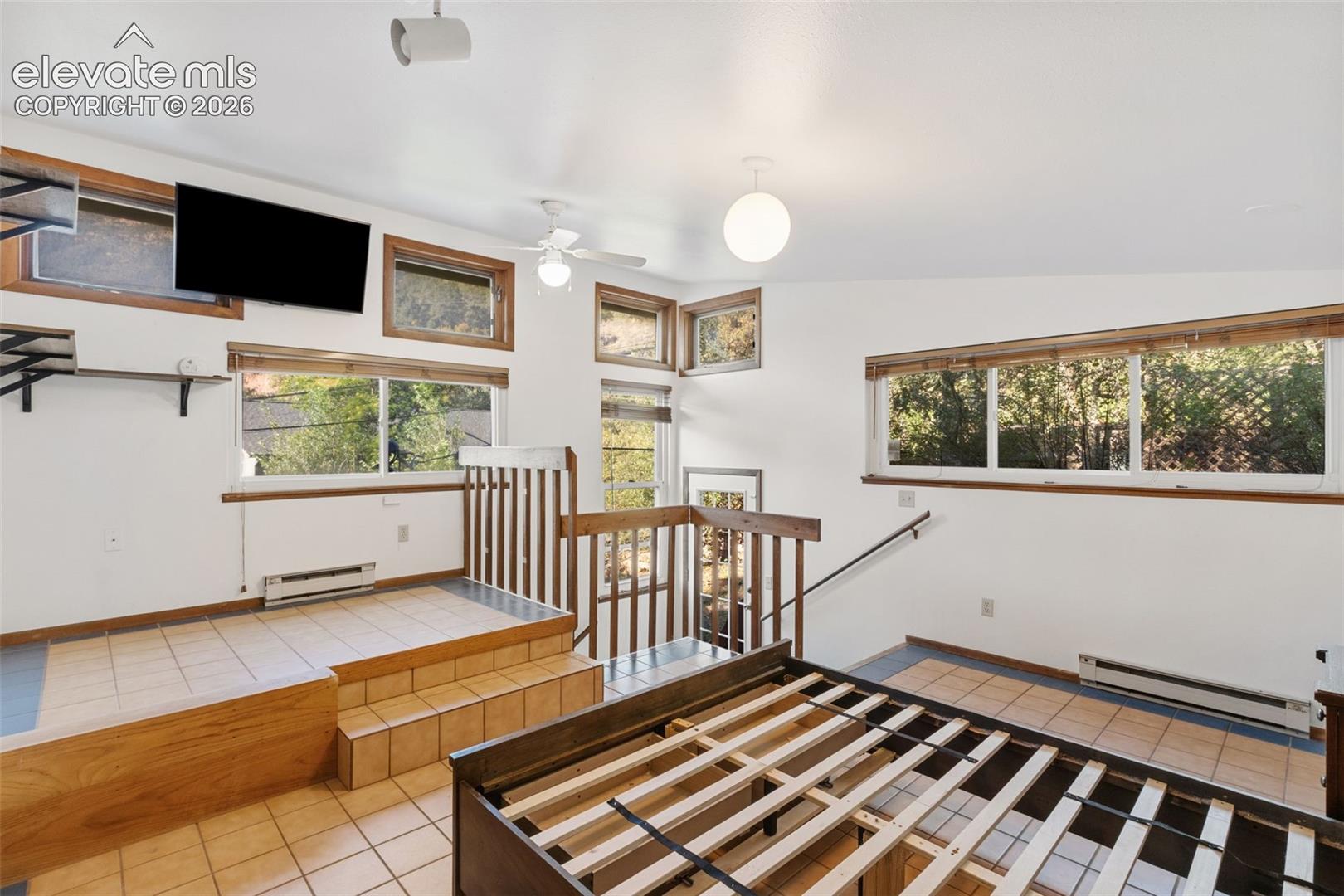 Multi-level living space featuring ceramic tile flooring, tiered floor platforms, natural wood trim, expansive windows, and a built-in wooden staircase railing