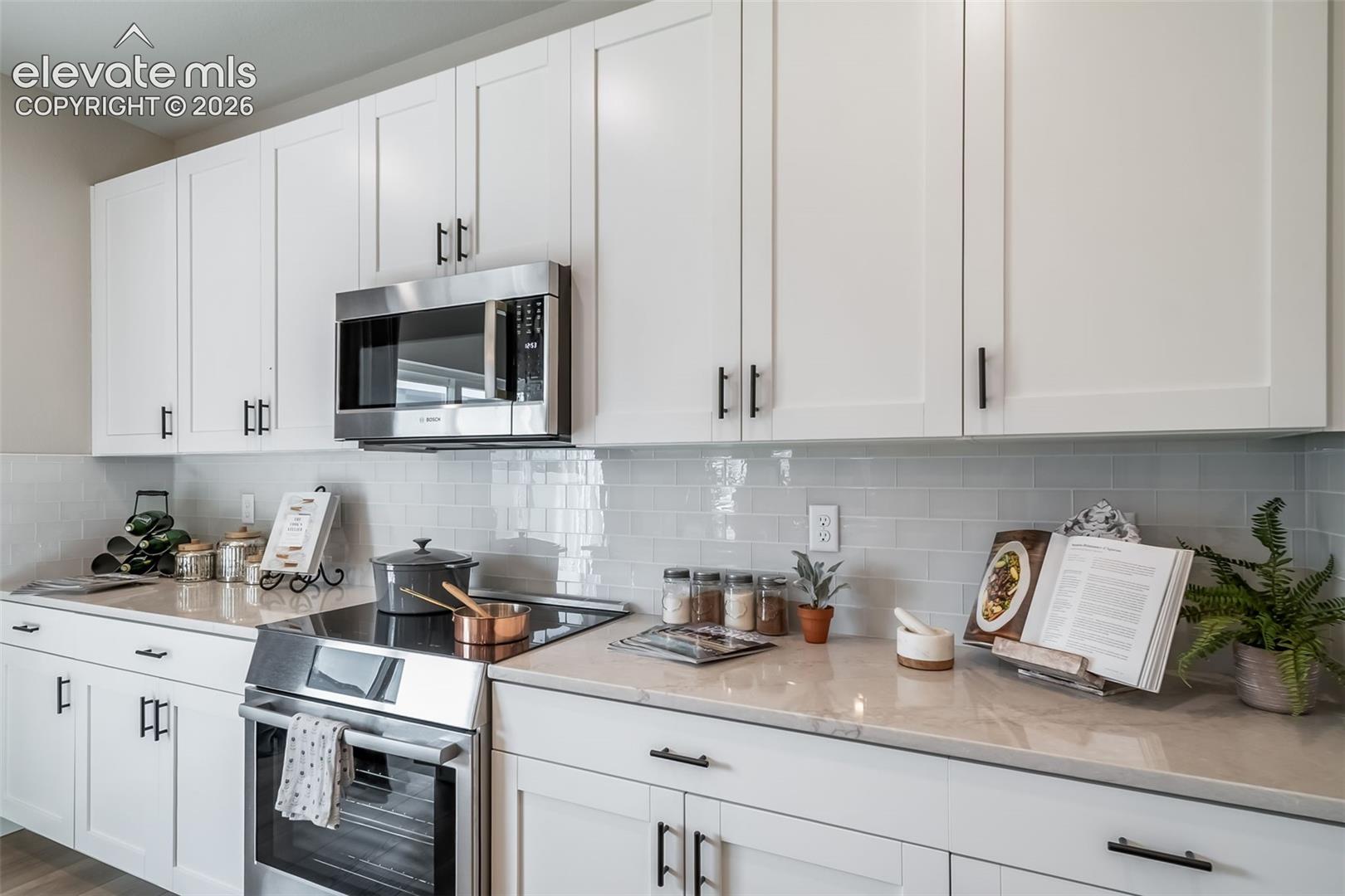Kitchen featuring extensive white shaker cabinetry, stainless steel appliances, light-toned countertops, and a subway tile backsplash
*Photos of a model home*