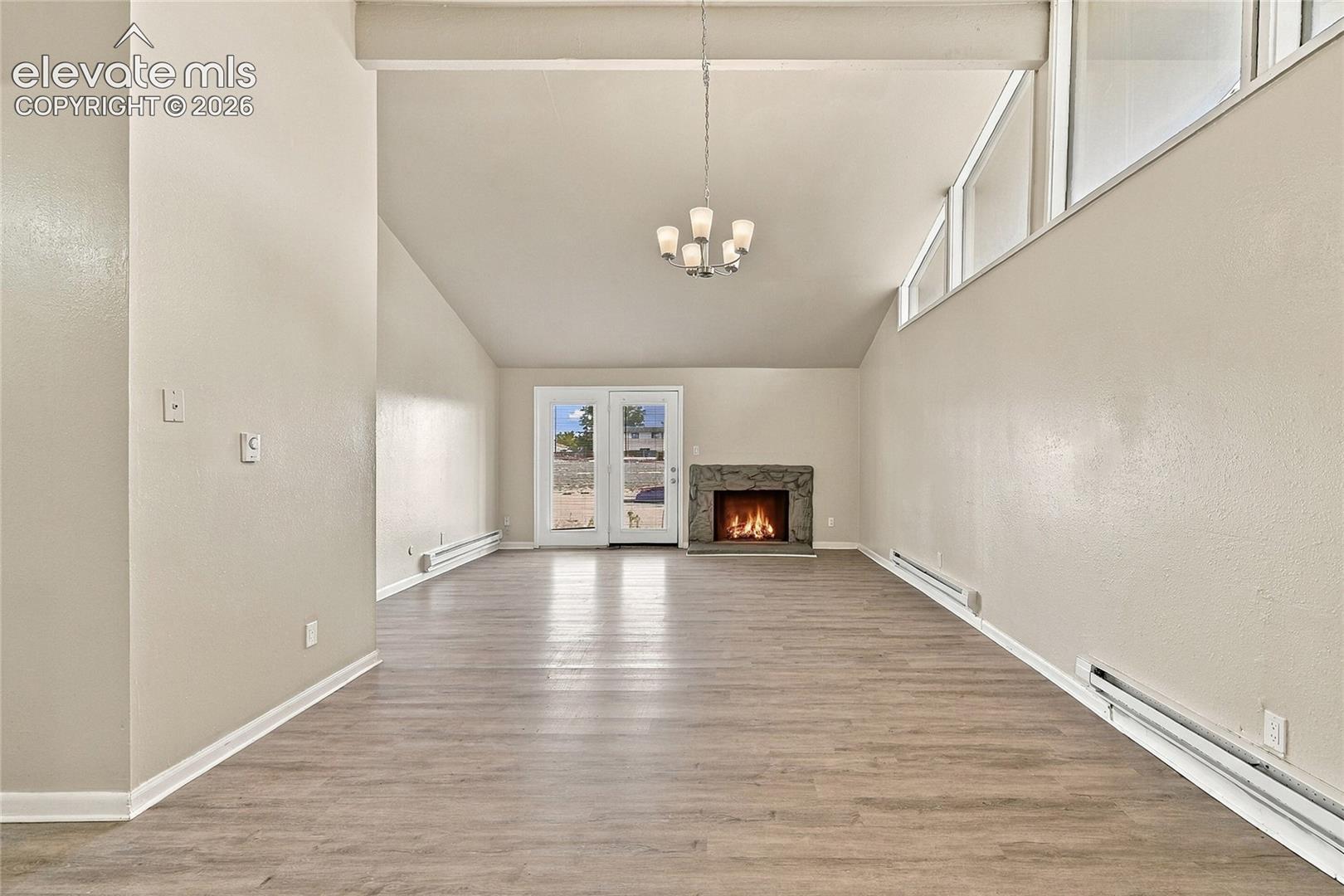 Vaulted ceilings featuring clerestory windows, stone-surround fireplace, wood-finish flooring, and multi-light hanging chandelier