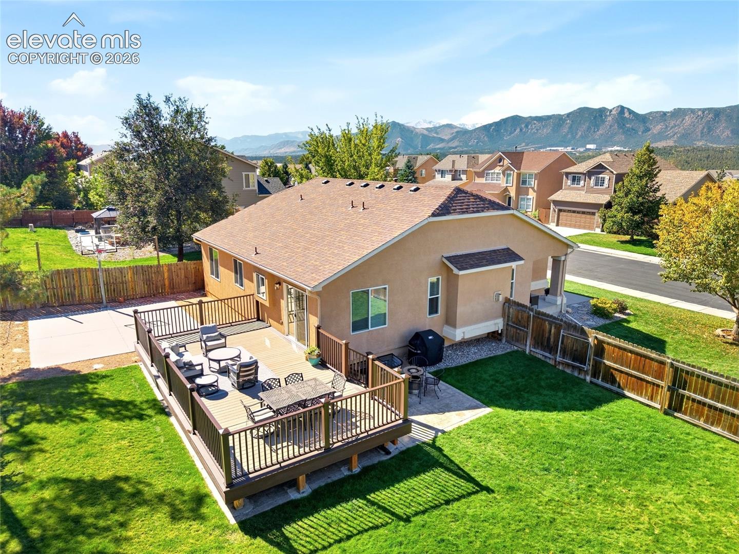 Expansive wood-finish deck, stucco exterior, paved patio, and a manicured lawn