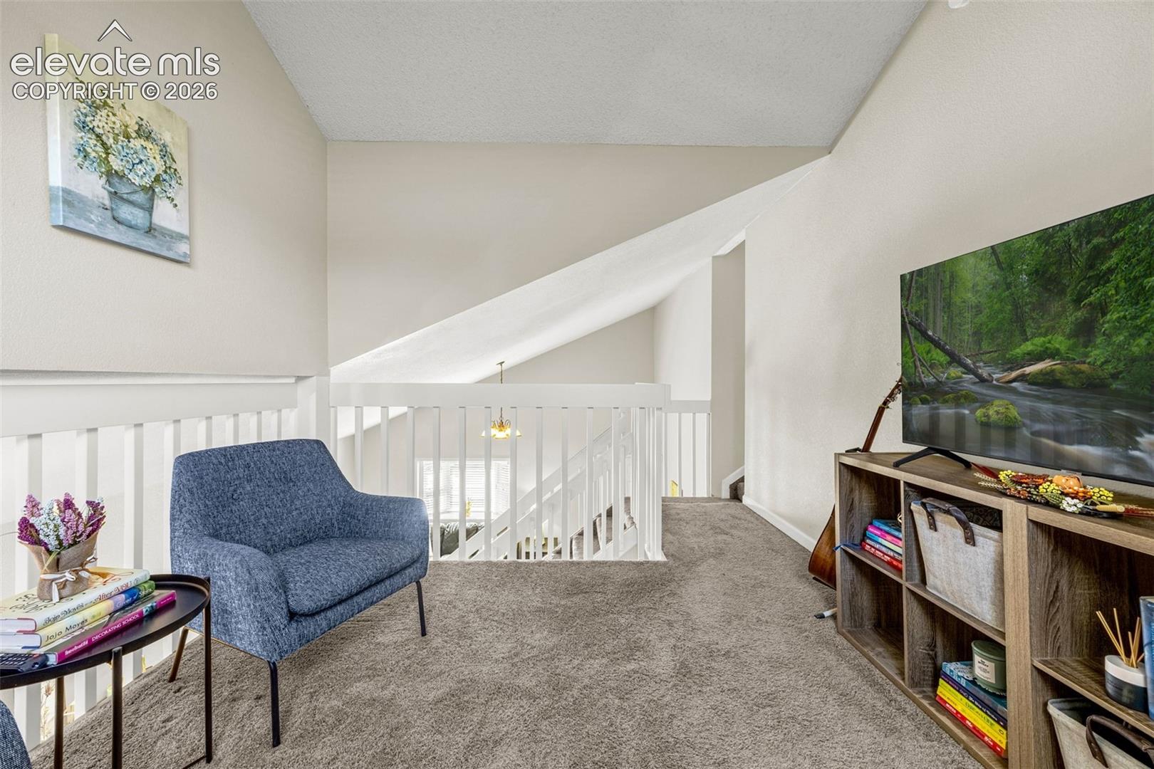 Vaulted ceiling with open-railing staircase balustrade and neutral wall-to-wall carpeting