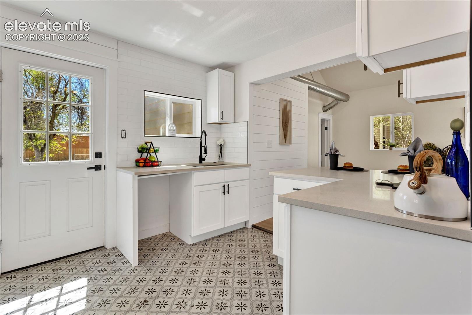 Kitchen featuring patterned floor tile, white shaker cabinetry, light-toned countertops, a black gooseneck faucet, and shiplap wall accents