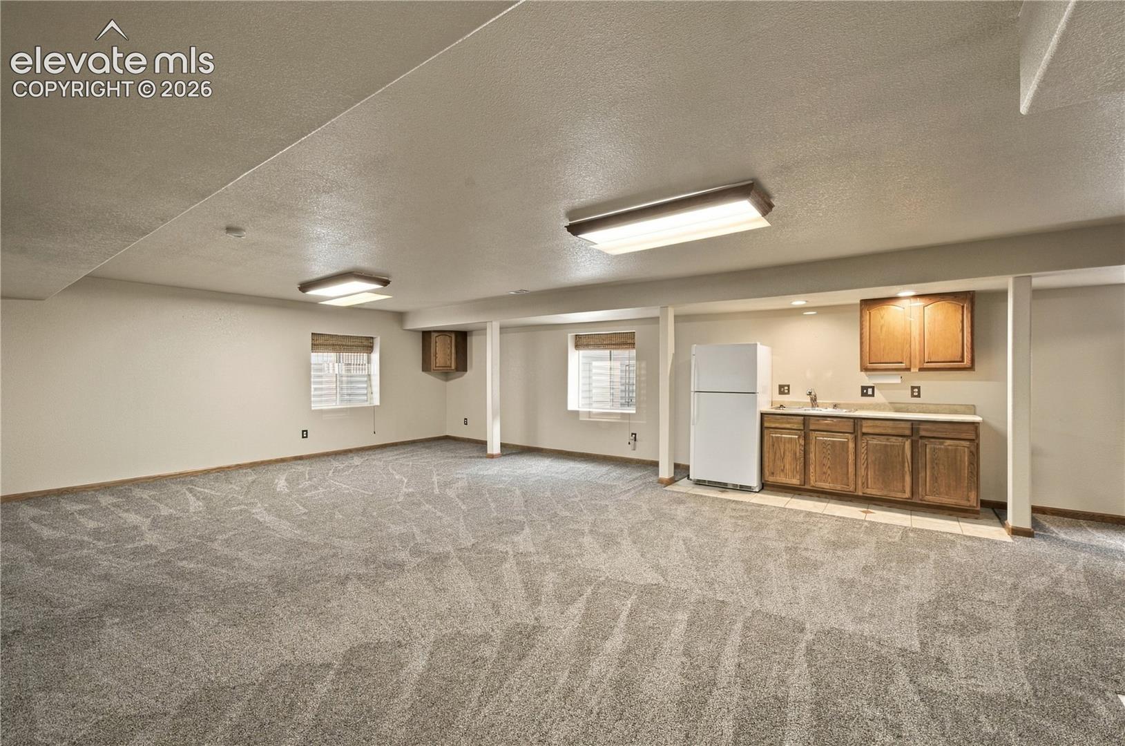 Open-concept area featuring wall-to-wall carpeting, wood-finish cabinetry, built-in sink, and two windows