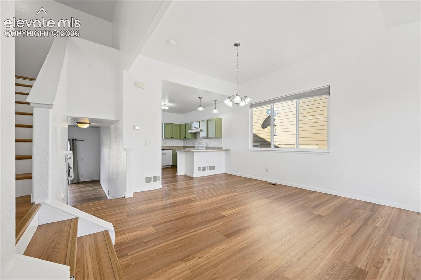 Open-concept interior featuring wood-finish flooring, vaulted ceilings, a kitchen with cabinetry, and a multi-tiered staircase