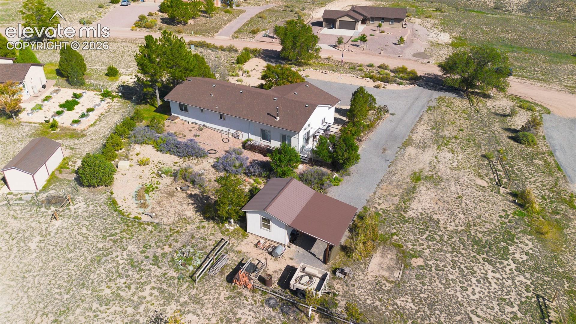 Aerial perspective of a sprawling property featuring a detached carport, a separate storage structure, a multi-section roofline, and established landscaping