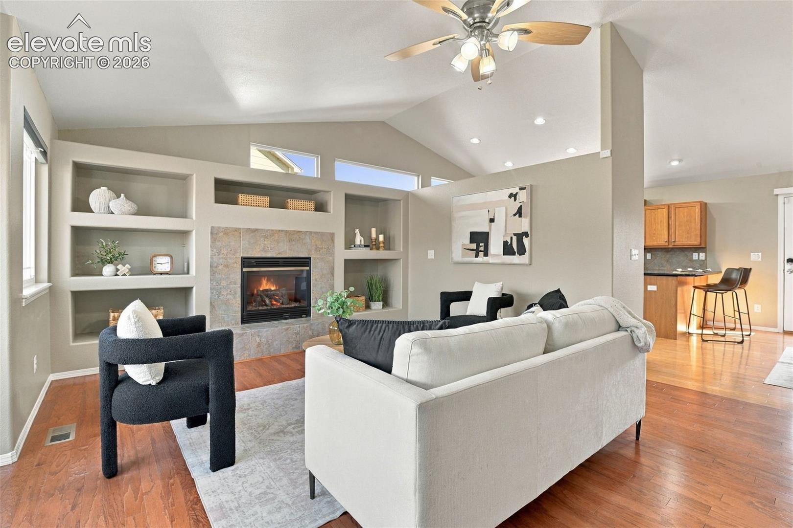 Vaulted ceiling, wood-finish flooring, built-in shelving, tiled fireplace, and recessed lighting