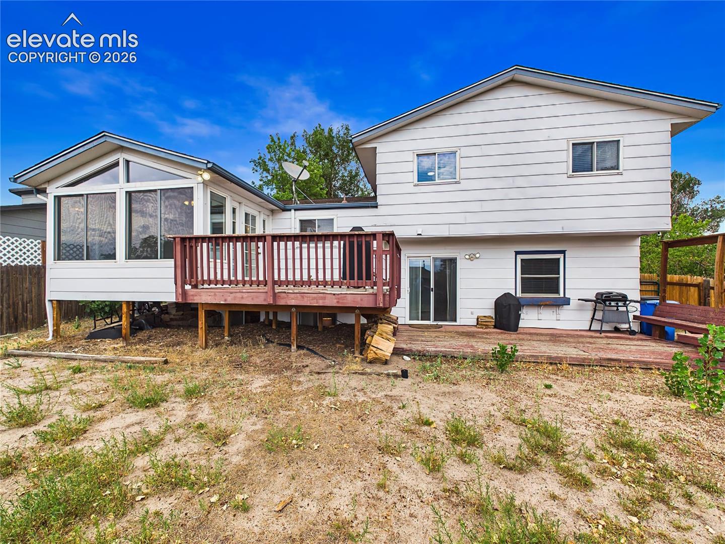 Backyard featuring a spacious deck, enclosed sunroom, and plenty of outdoor space for relaxing or entertaining.