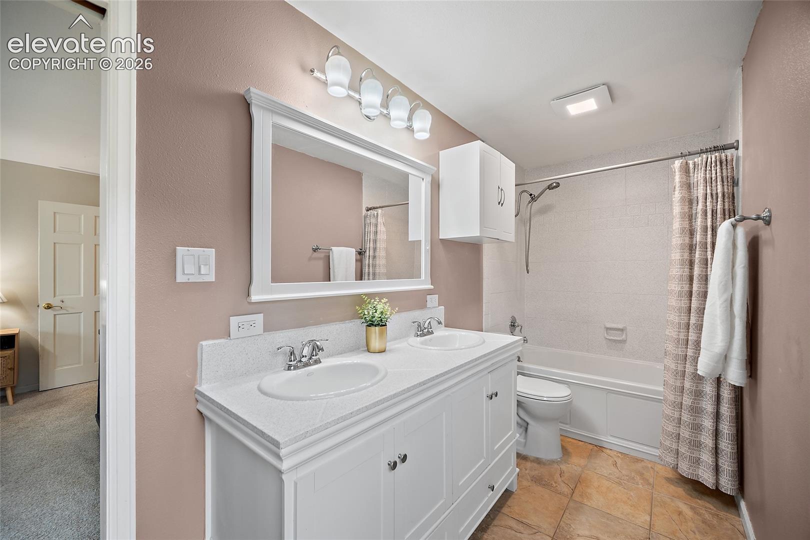 Dual-sink vanity with white cabinetry and light-toned countertop, framed wall mirror, four-light vanity fixture, and tiled tub and shower combination