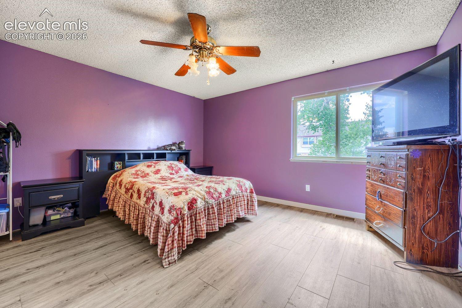 Wood-finish flooring, ceiling fan with integrated lighting, built-in headboard with shelving, window with natural light