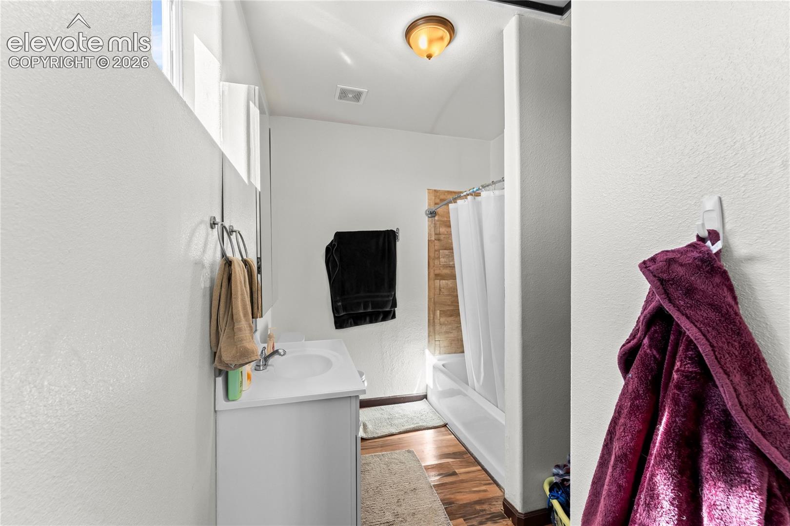 Bathroom featuring a white vanity cabinet, integrated sink, wood-finish flooring, and a tiled shower surround