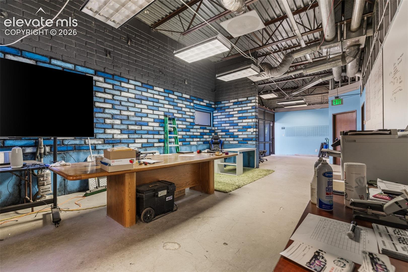 Industrial-style space featuring exposed metal ceiling joists and ductwork, painted brick walls, recessed fluorescent lighting, and polished concrete flooring