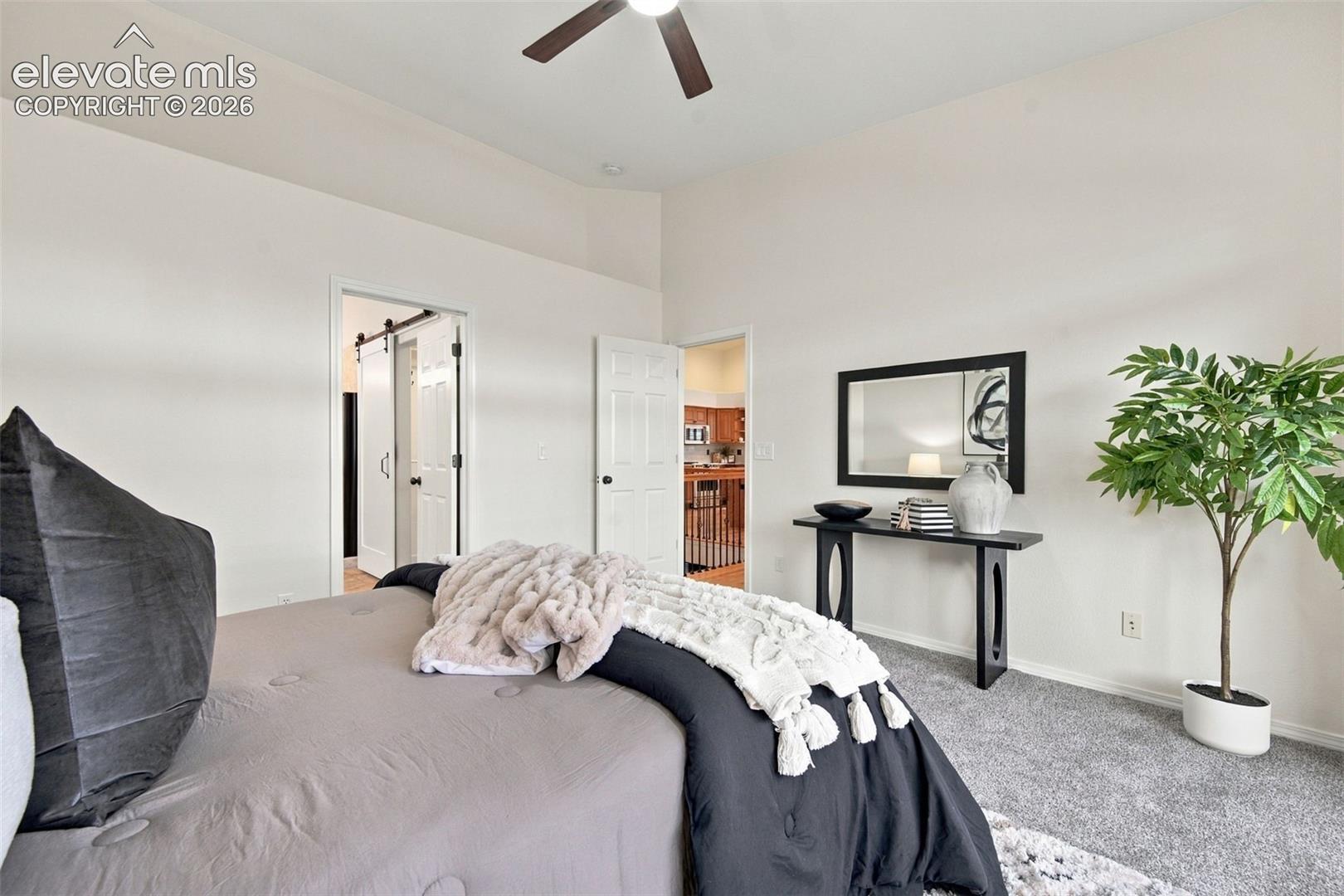 Vaulted ceiling featuring a central lighted ceiling fan, neutral carpeting, and a sliding barn-style door