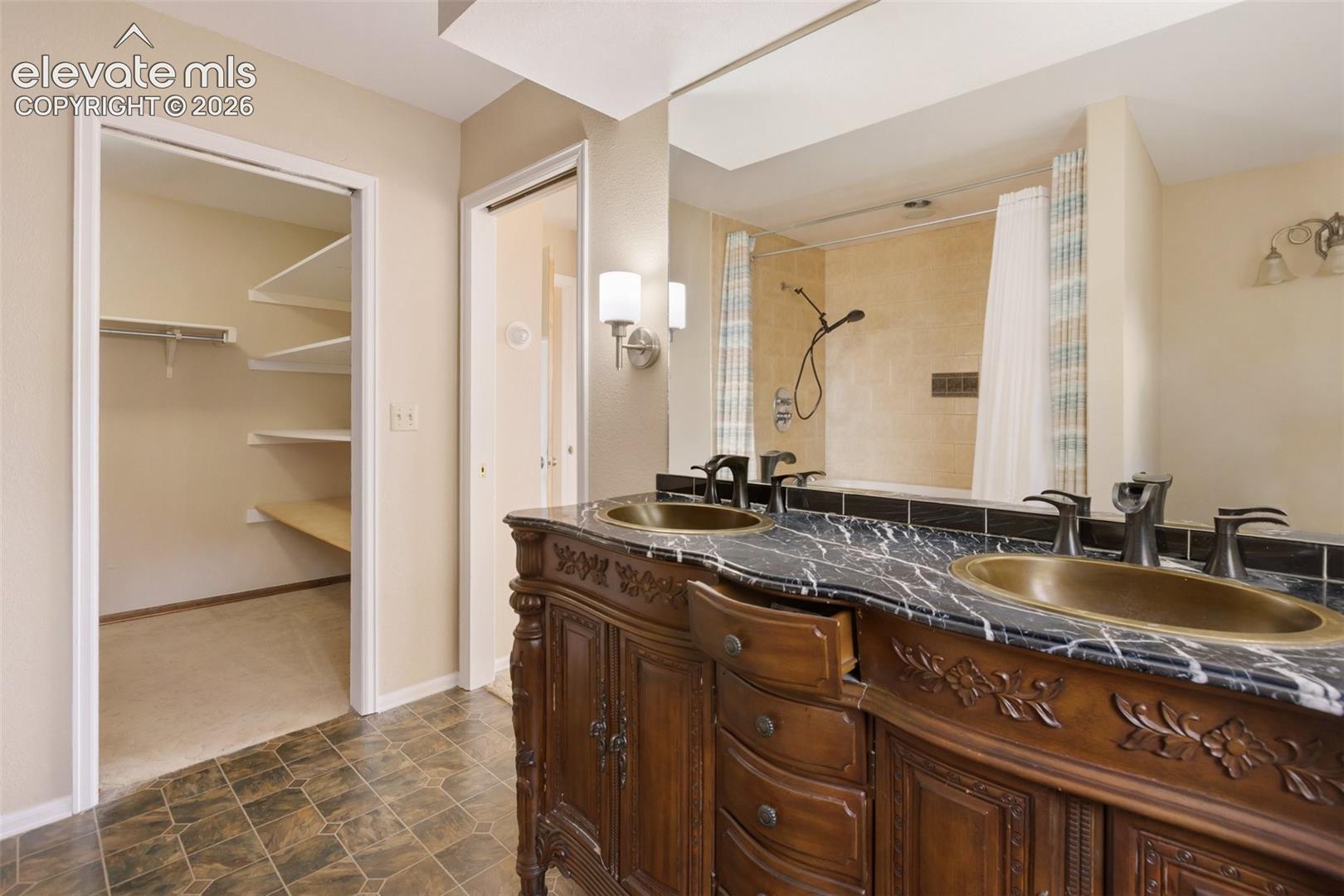 Dual vanity with dark stone countertop, ornate wood cabinetry, and vessel sinks
