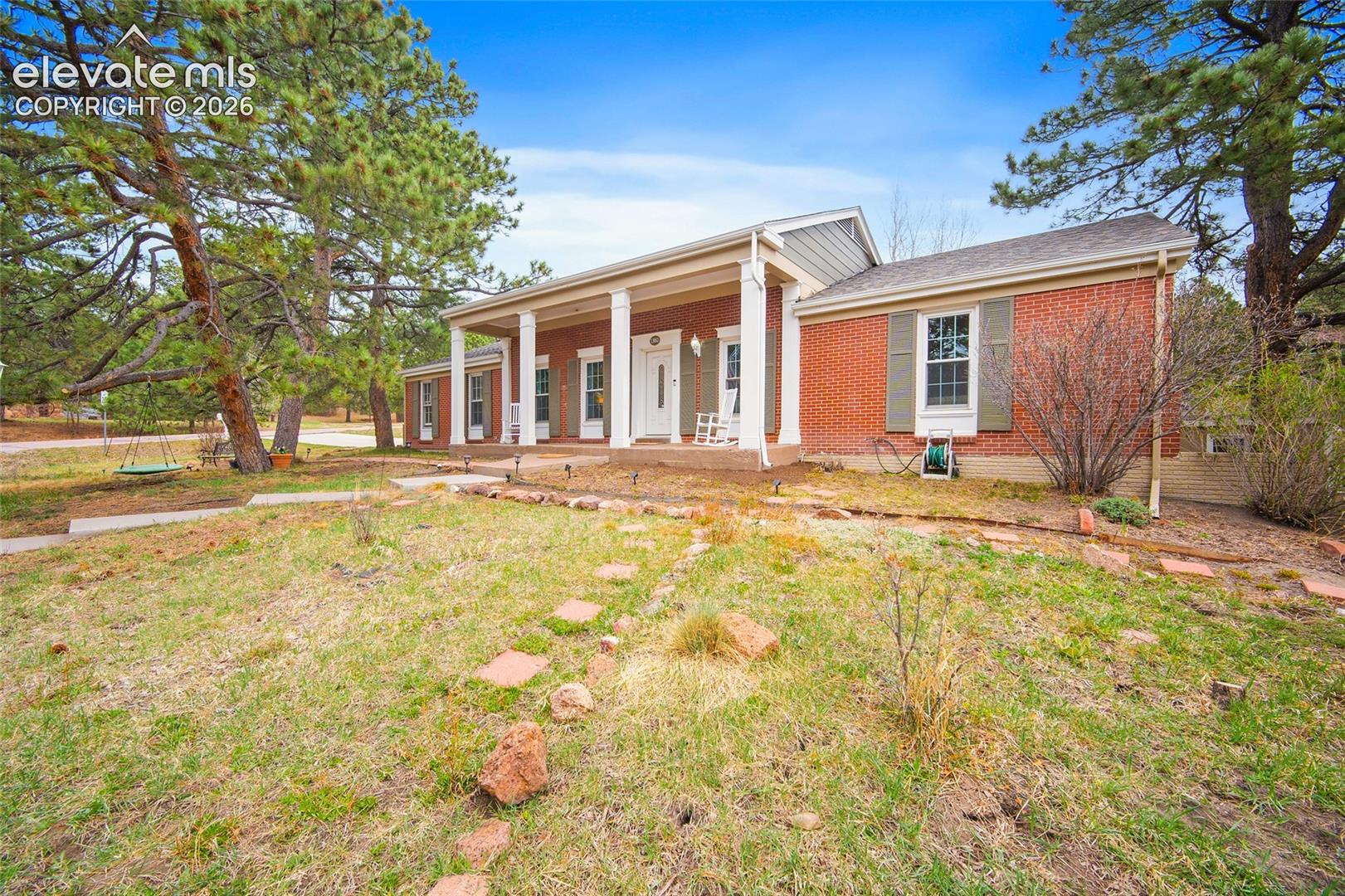 Red brick exterior featuring a covered front porch with white columns, window shutters, and a walkway composed of stone pavers