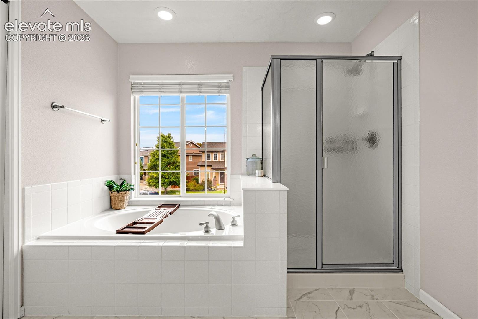 Soaking tub with a tile-surround deck, glass-enclosed shower, tile flooring, and a window with a blind