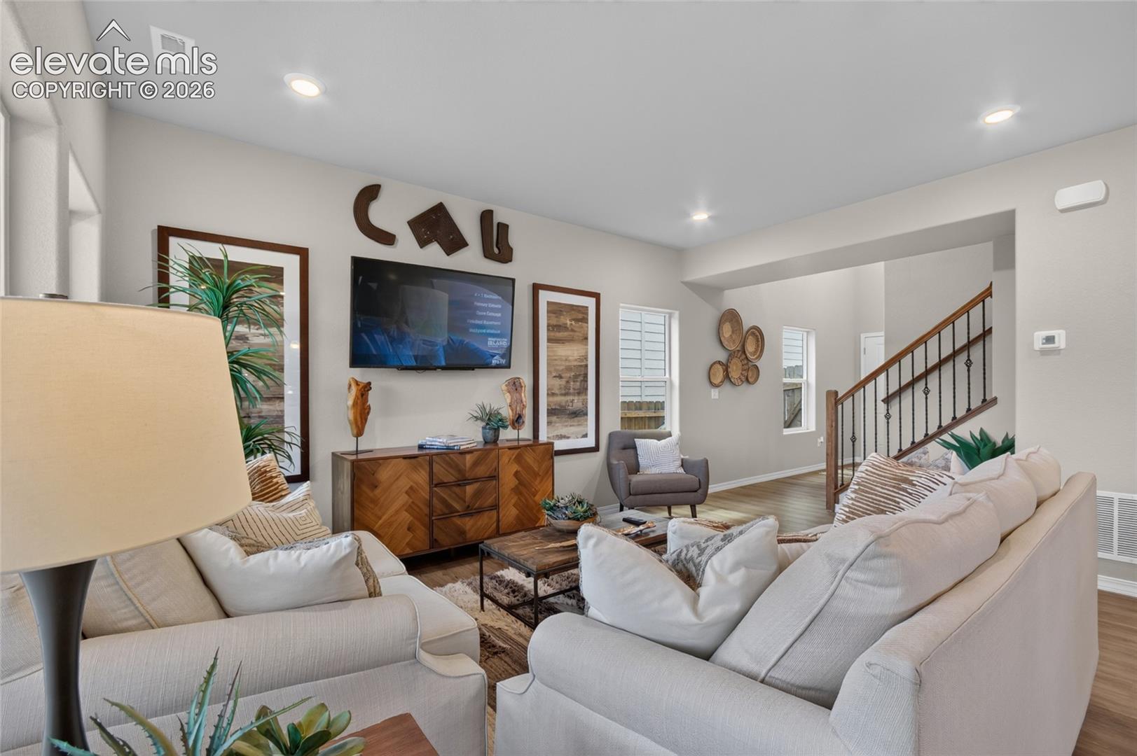 Living space featuring recessed lighting, wood-finish flooring, and a staircase with a wooden handrail and metal balusters