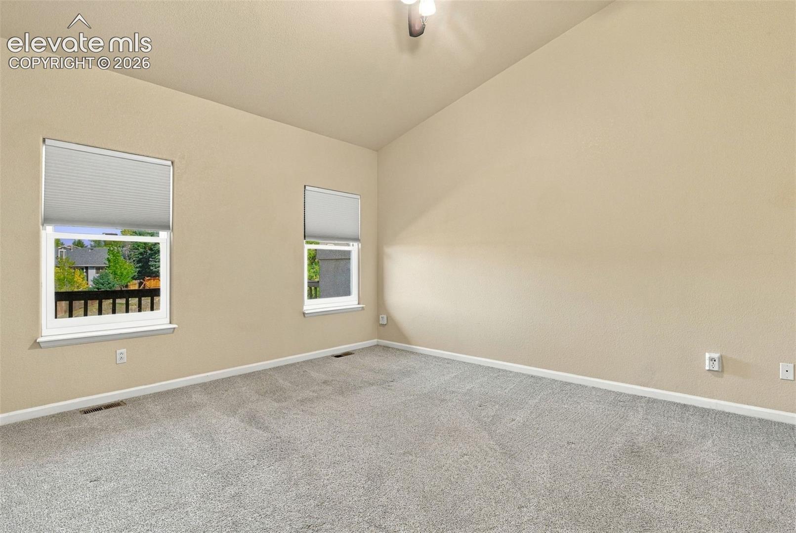 Vaulted ceiling, neutral wall tones, wall-to-wall carpeting, and dual windows with fitted cellular shades