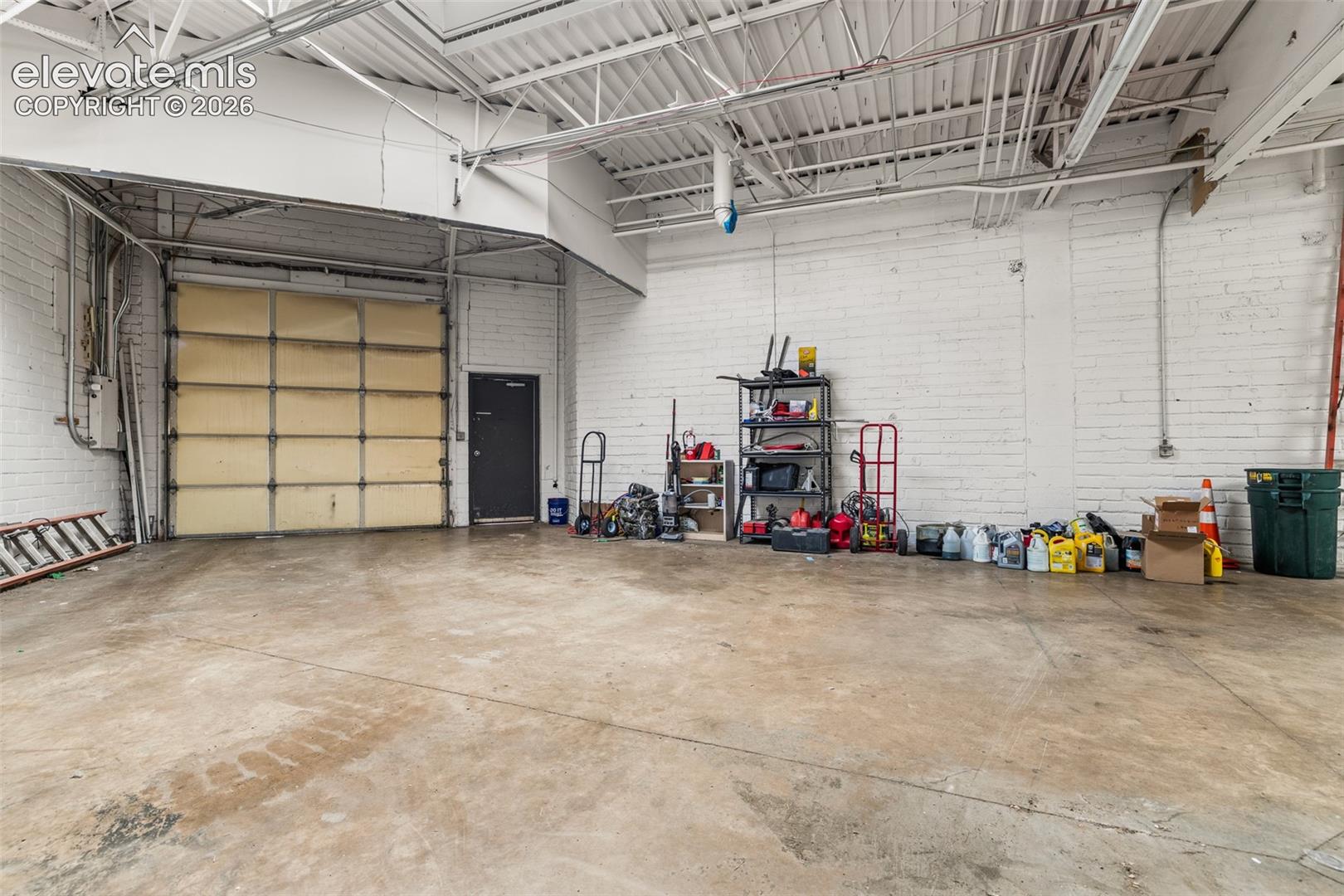 Industrial space featuring high vaulted ceilings, concrete flooring, painted masonry walls, and a large roll-up service door