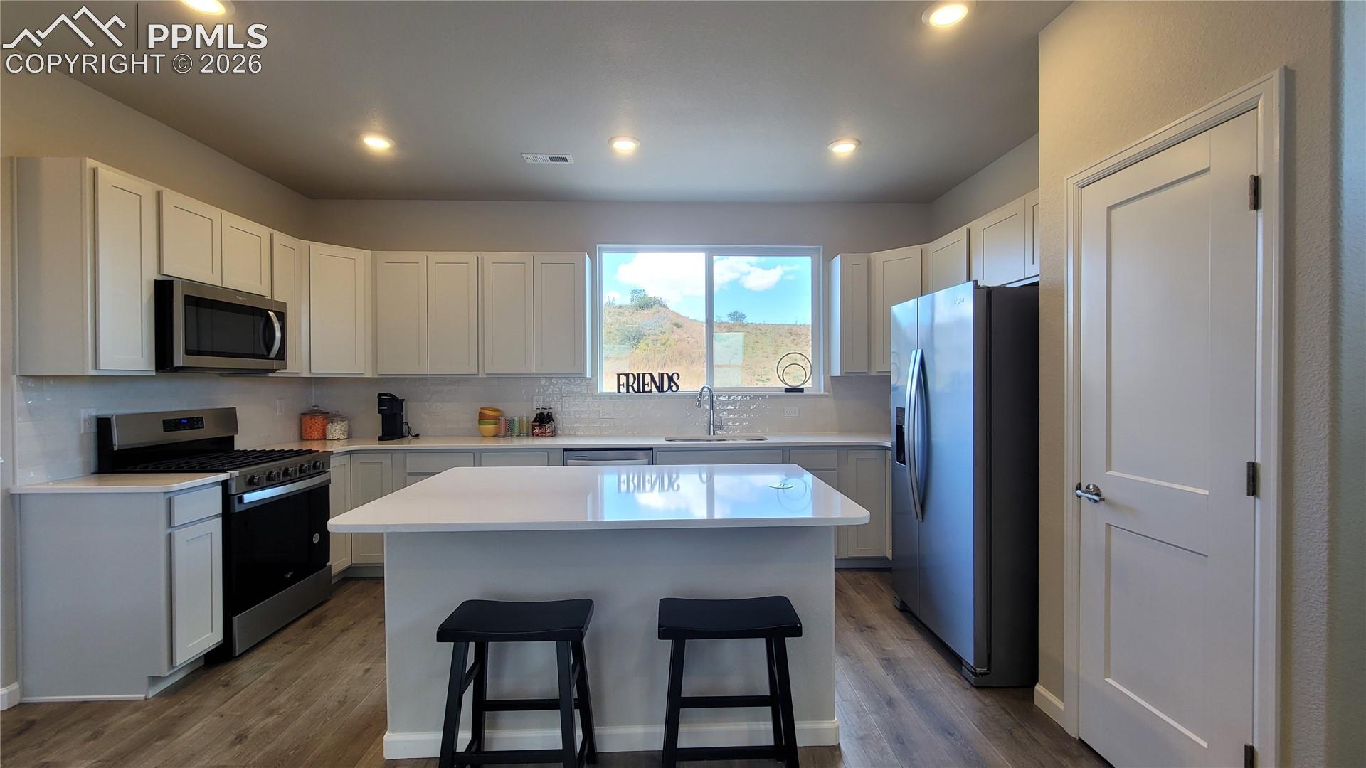 Kitchen with Quartz countertop, pantry, island providing additional seating, and stainless steel gas range, microwave, and dishwasher! 