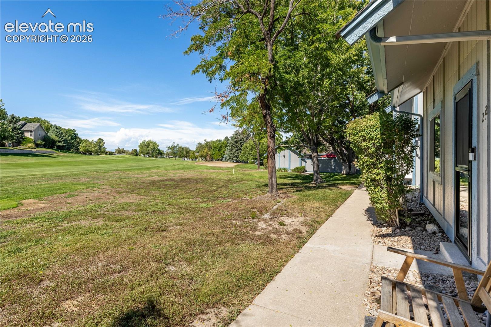 Exterior property grounds featuring a concrete walkway, mature trees, and open grass expanse