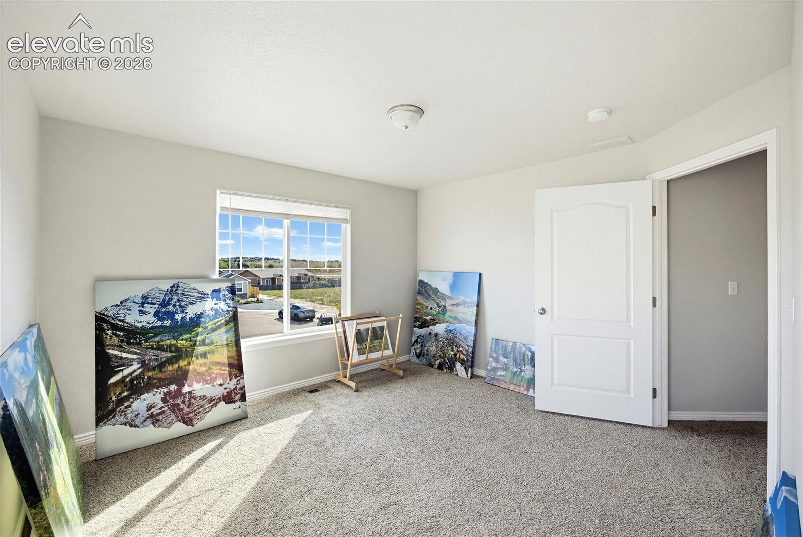 Neutral-toned interior space featuring neutral wall paint, wall-to-wall carpeting, a multi-pane window, and a white two-panel interior door