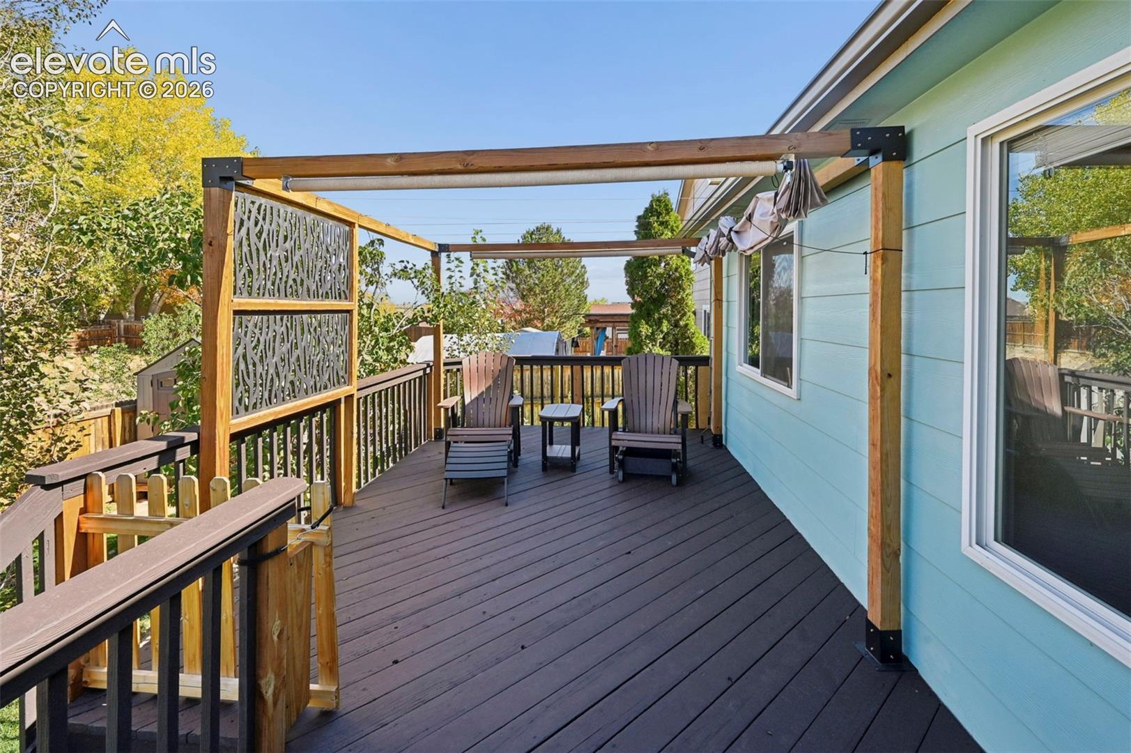 Elevated deck featuring wood-finish flooring, black railing, a timber-frame pergola, and decorative metal privacy screening