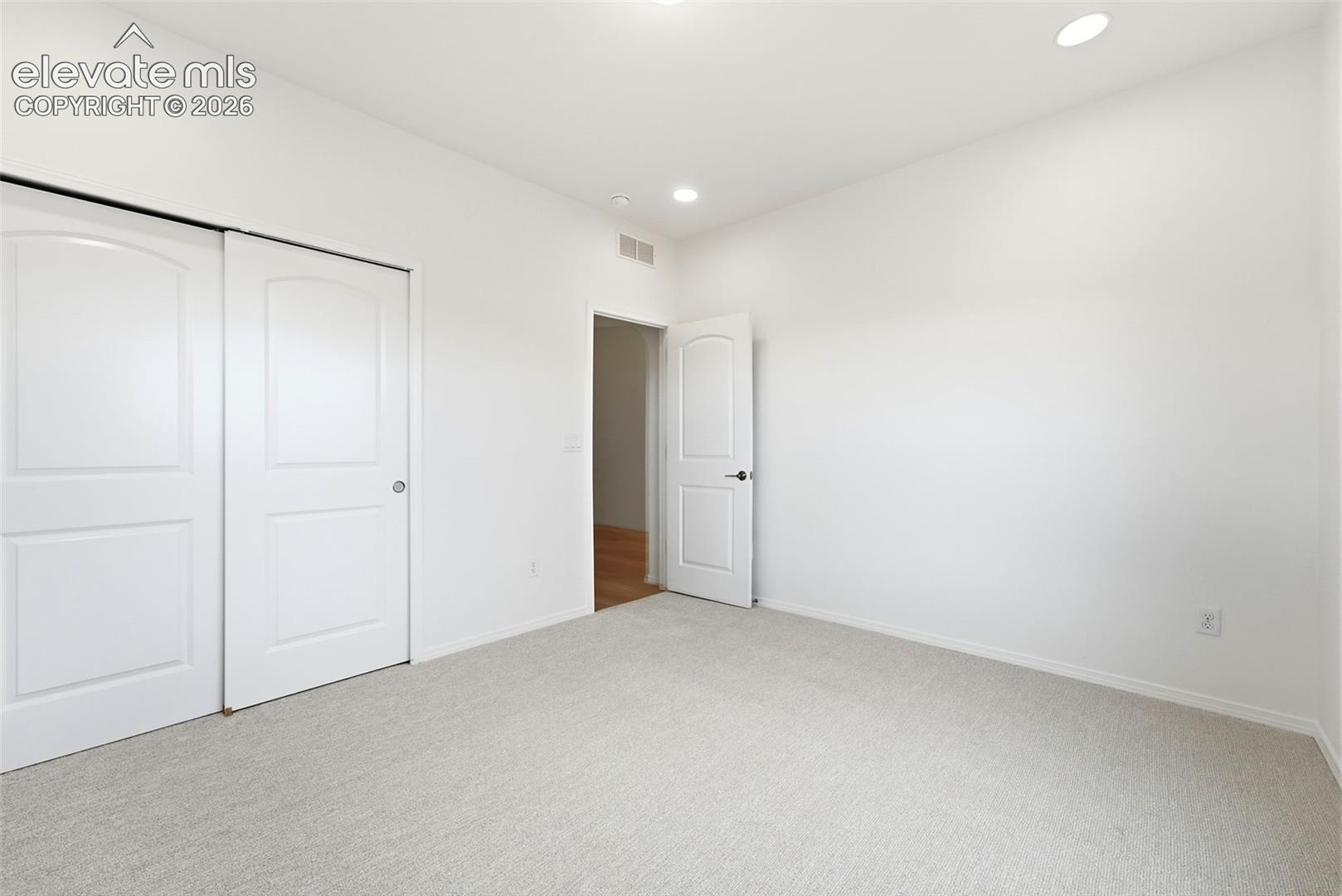 Neutral-toned carpeting, recessed ceiling lighting, arched two-panel interior doors, and sliding closet doors