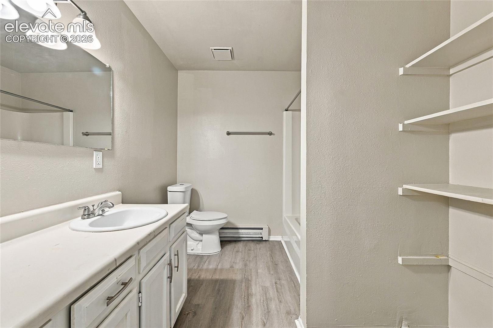 Bathroom featuring a vanity with a solid-surface countertop, an integrated sink, wood-finish flooring, built-in shelving, and a tub-shower combination