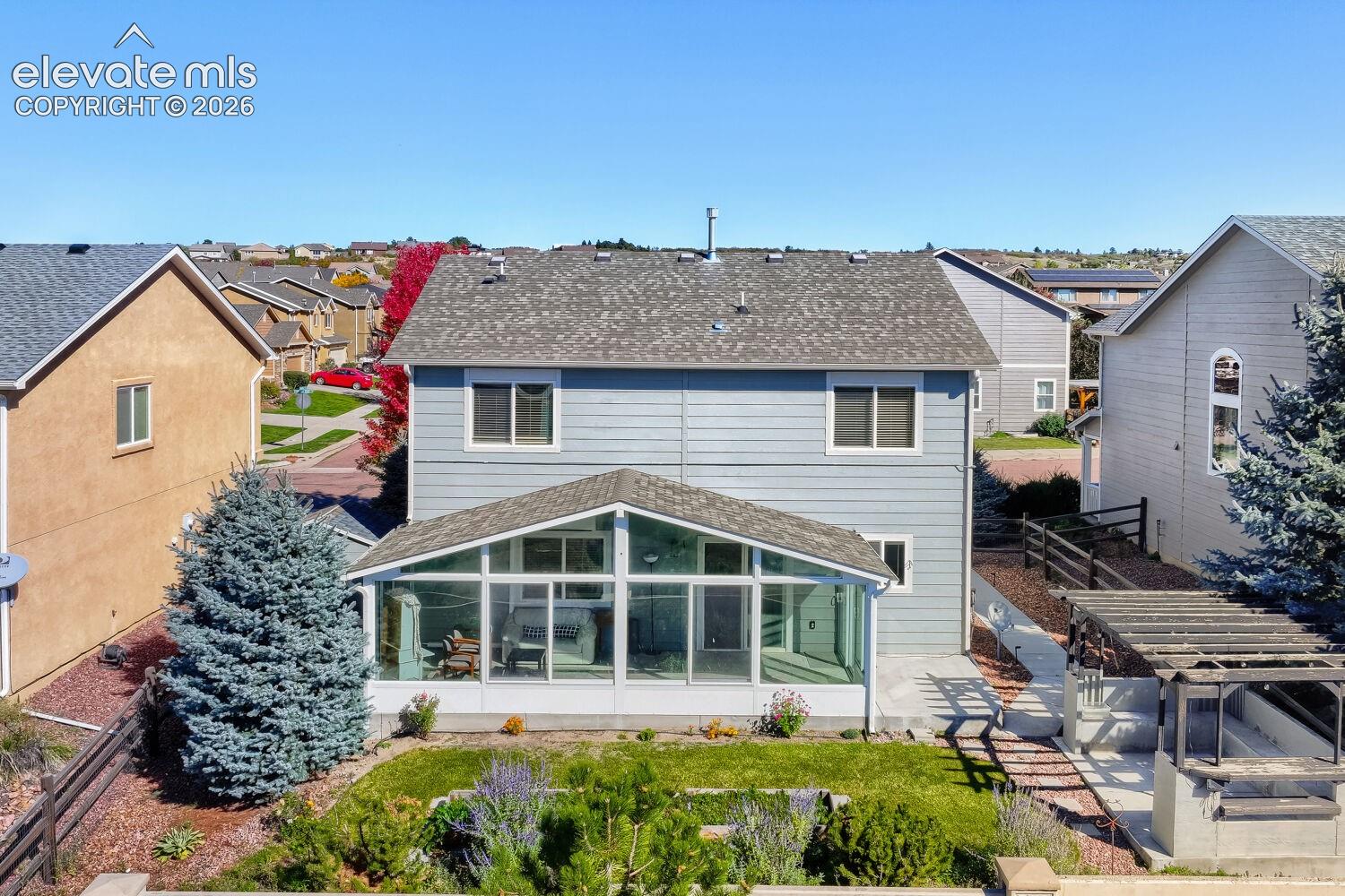 Two-story residence featuring horizontal lap siding, a glass-enclosed sunroom, a backyard patio area with a wooden pergola, and established landscaping