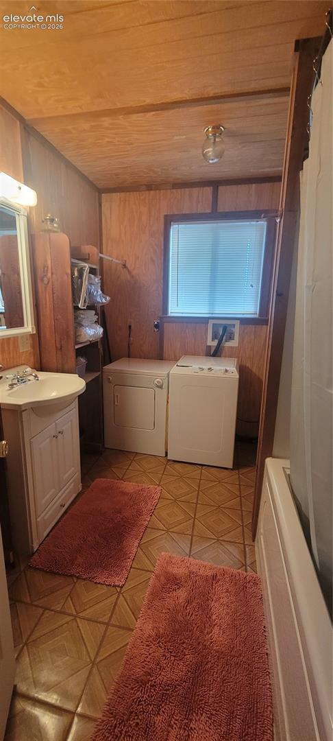 White vanity with a basin sink, wood-finish paneling, patterned flooring, and a window with blinds