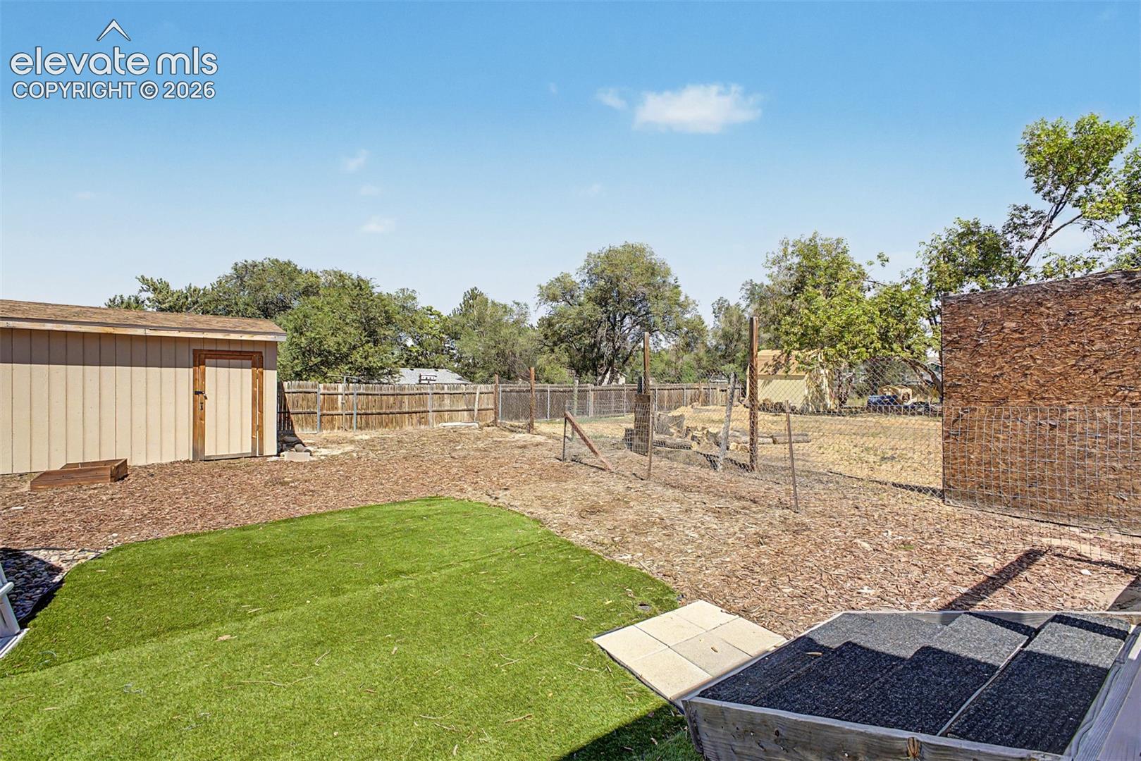Expansive backyard featuring artificial turf, a large shed and fencing. 