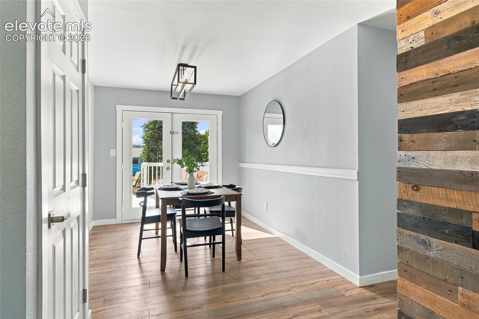 Interior space featuring wood-finish flooring, a horizontal wood-plank accent wall, chair rail molding, and a geometric-frame ceiling light fixture, complete with glass-paneled french doors