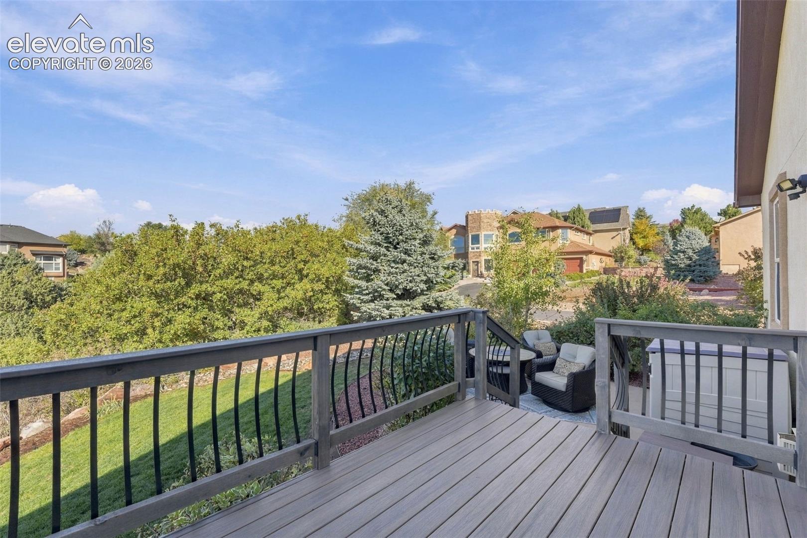 Elevated wooden deck featuring metal balusters, grass lawn, mature trees, and landscaping elements