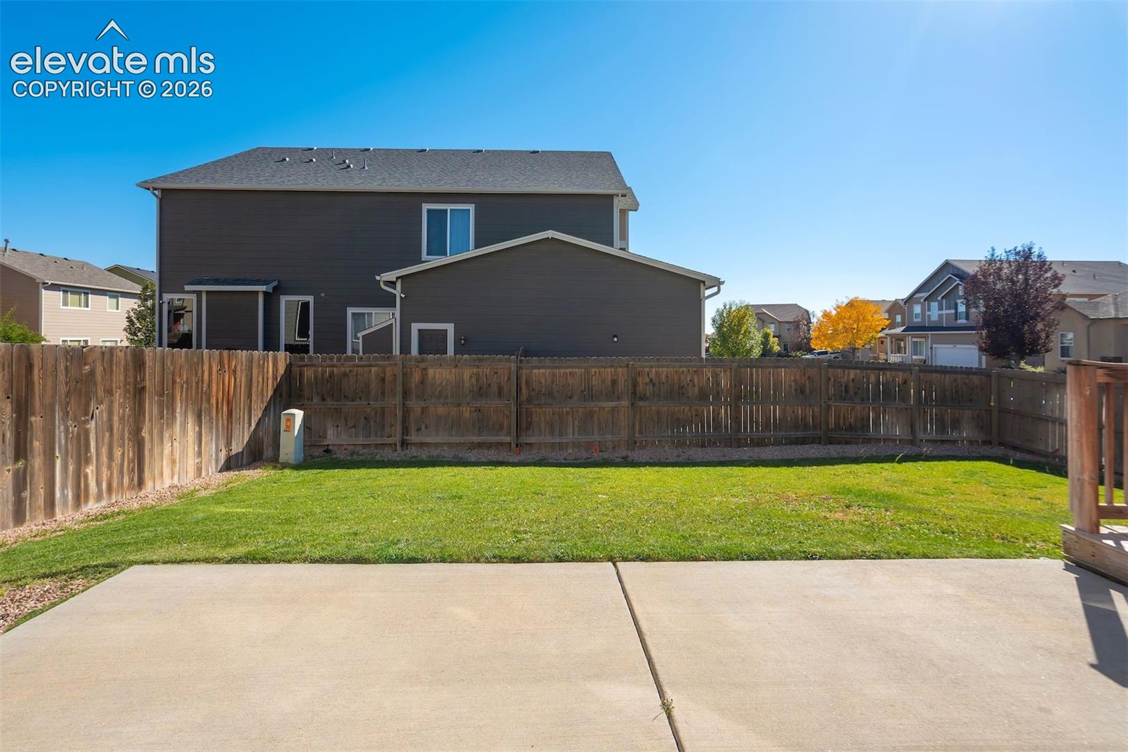 Expansive backyard featuring a manicured lawn, concrete patio, and full perimeter wood fencing