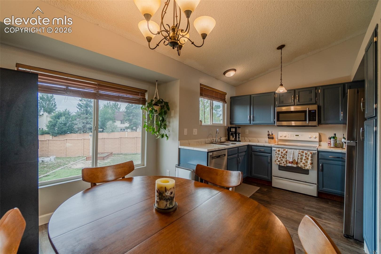 Kitchen featuring wood-finish flooring, white countertops, blue cabinetry, stainless steel appliances, and a vaulted ceiling