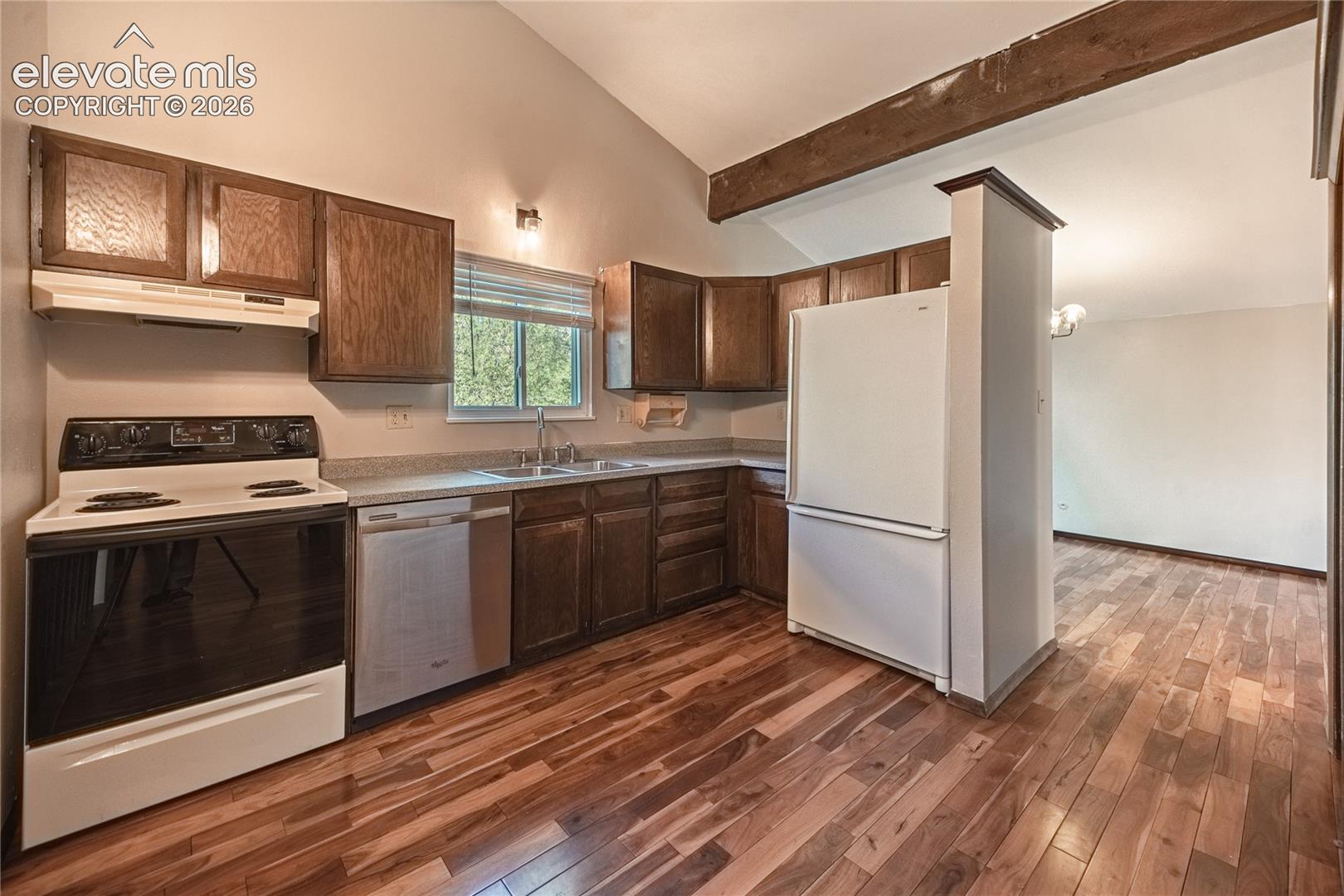 Kitchen featuring wood-finish cabinetry, stone-texture countertops, wood-finish flooring, a vaulted ceiling, and an exposed structural wood beam