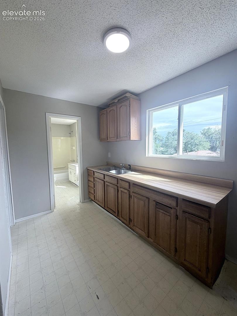 Wood-finish cabinetry with a double basin stainless steel sink and laminate countertops, complemented by an overhead light fixture
