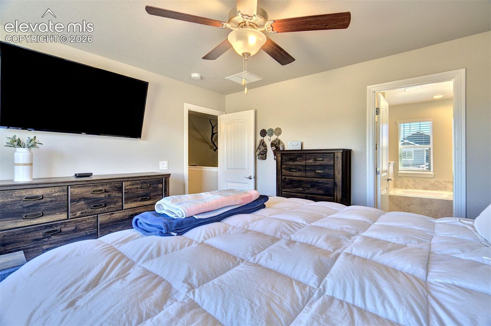 Neutral-toned interior featuring a ceiling fan with integrated lighting, multi-panel doors, and an archway revealing a bathroom with a soaking tub