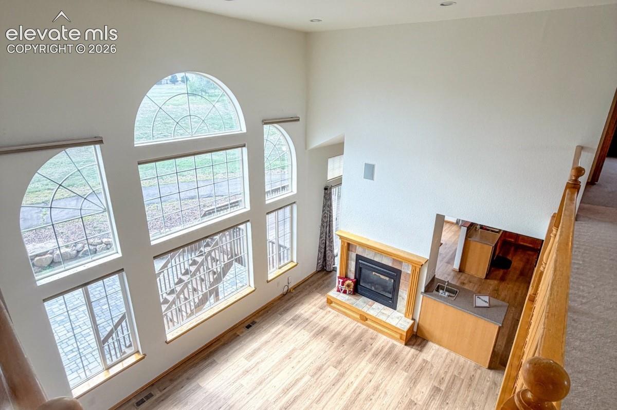 Two-story vaulted ceiling with large arched windows, wood-finish flooring, and a fireplace with a tile surround and wood mantel. No staging.
