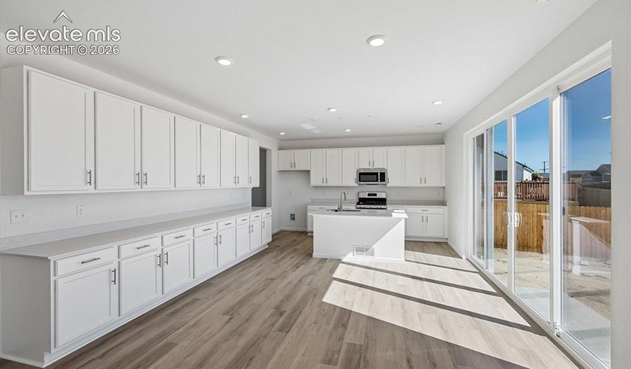 Kitchen featuring white cabinetry, wood-finish flooring, recessed lighting, center island, and glass sliding doors