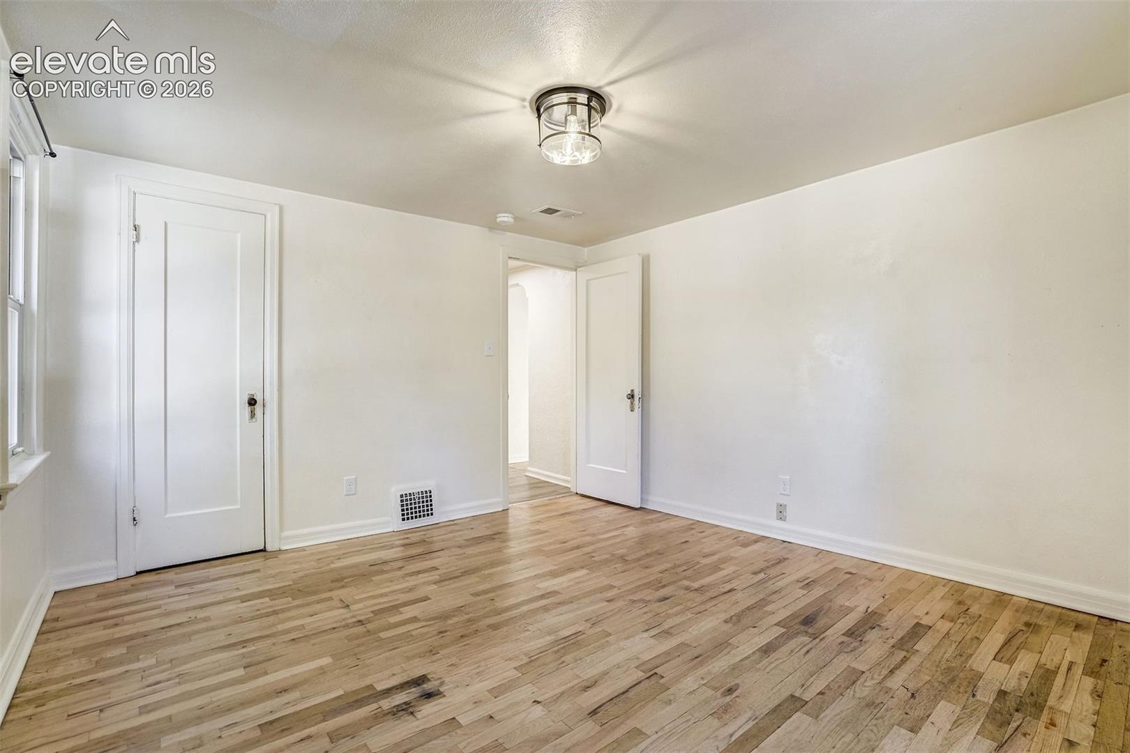 Interior room featuring wood-finish flooring, two classic panel doors with brass-toned hardware, and a semi-flush mount ceiling fixture with a metallic frame